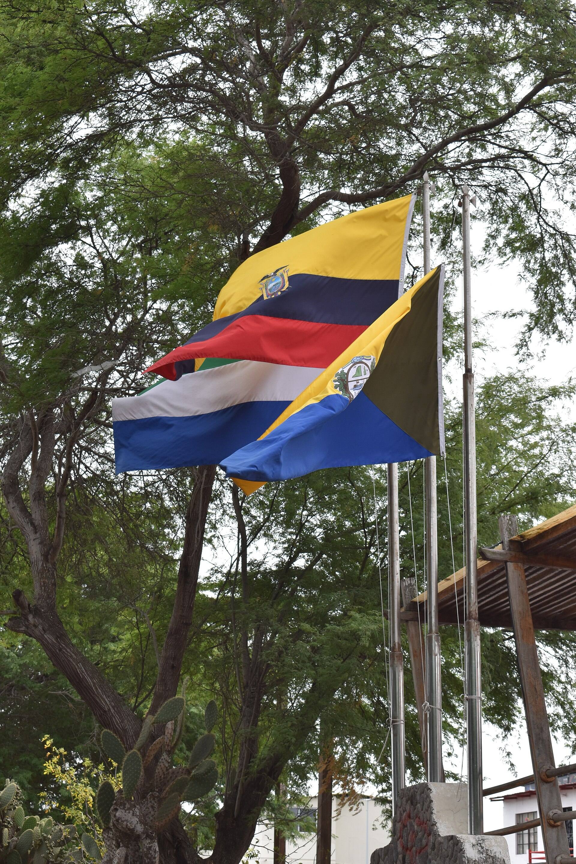 Ecuador, Galápagos and Puerto Baquerizo Moreno flags beside trees on the waterfront